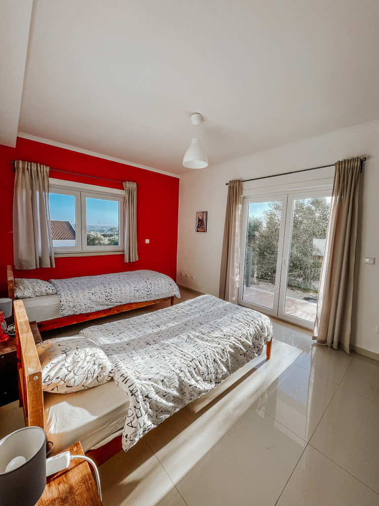 Bright twin bedroom with red accent wall and glass doors to the garden