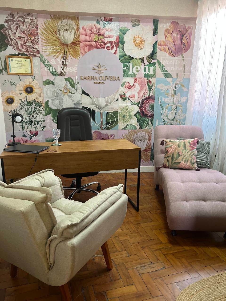Consultório do Religare 381, com mesa de madeira, poltrona bege, chaise rosa e painel floral na parede